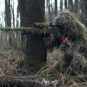 A Soldier Sniper Aiming Though The Rifle Scope In Forest