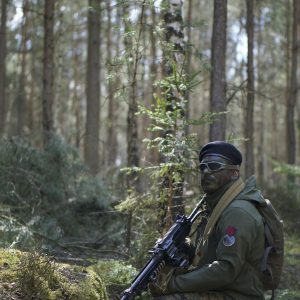 Man in Green Jacket Holding a Black Rifle in Forest