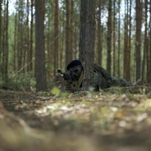 Man in Military Uniform  and a Backpack Lying on Ground Surrounded by Trees